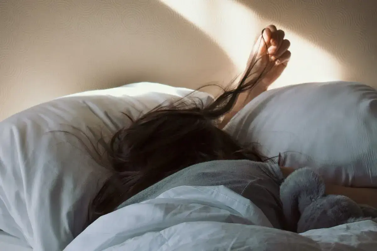 A person sleeps soundly, their hair spread across a pillow. The morning sun casts a warm glow, but the pillow rash is evident.