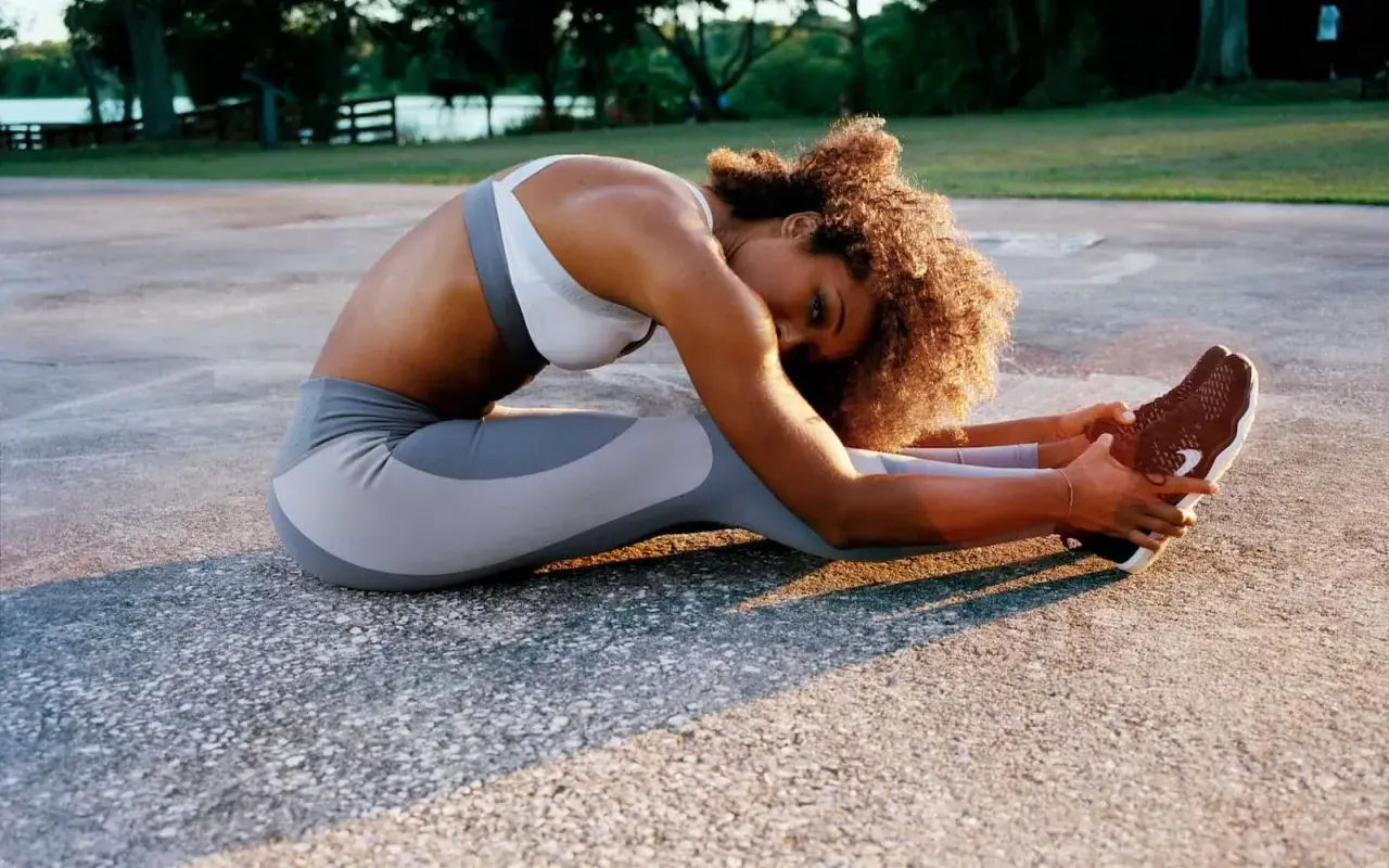 Femme en tenue de sport pratiquant une posture de yoga anti-stress, étirant ses jambes sur un sol extérieur.