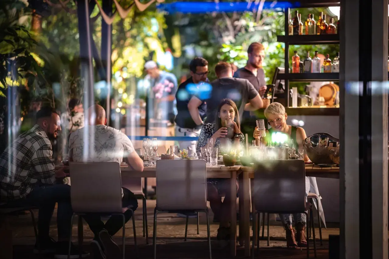 Ludzie siedzą przy stole w restauracji Olivia Business Centre, pijąc i rozmawiając.