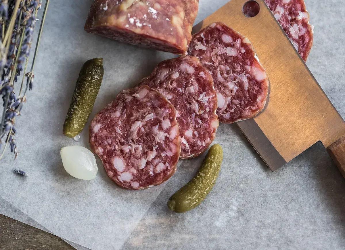 Plasterki salami z widocznym tłuszczem, ogórki konserwowe i cebulka. Salami jest z mięsa wieprzowego i wołowego.