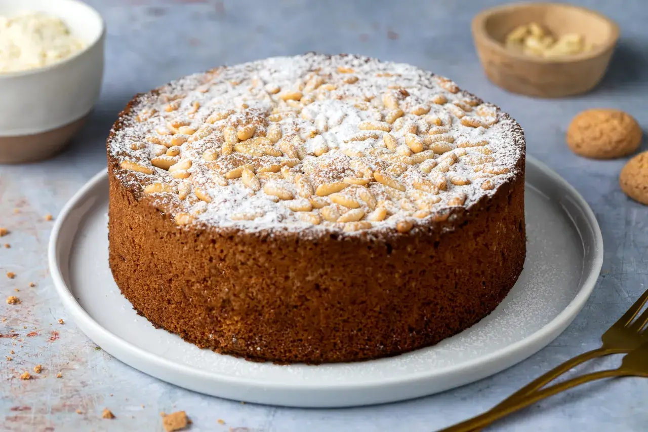 Torta rustica con farina di mandorle, cosparsa di zucchero a velo e pinoli tostati. Un dolce invitante, perfetto per ogni occasione.