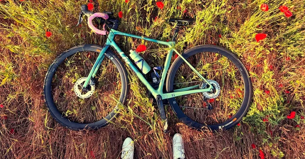 Zielony rower leżący na łące pełnej maków, z widocznymi butami rowerowymi.
