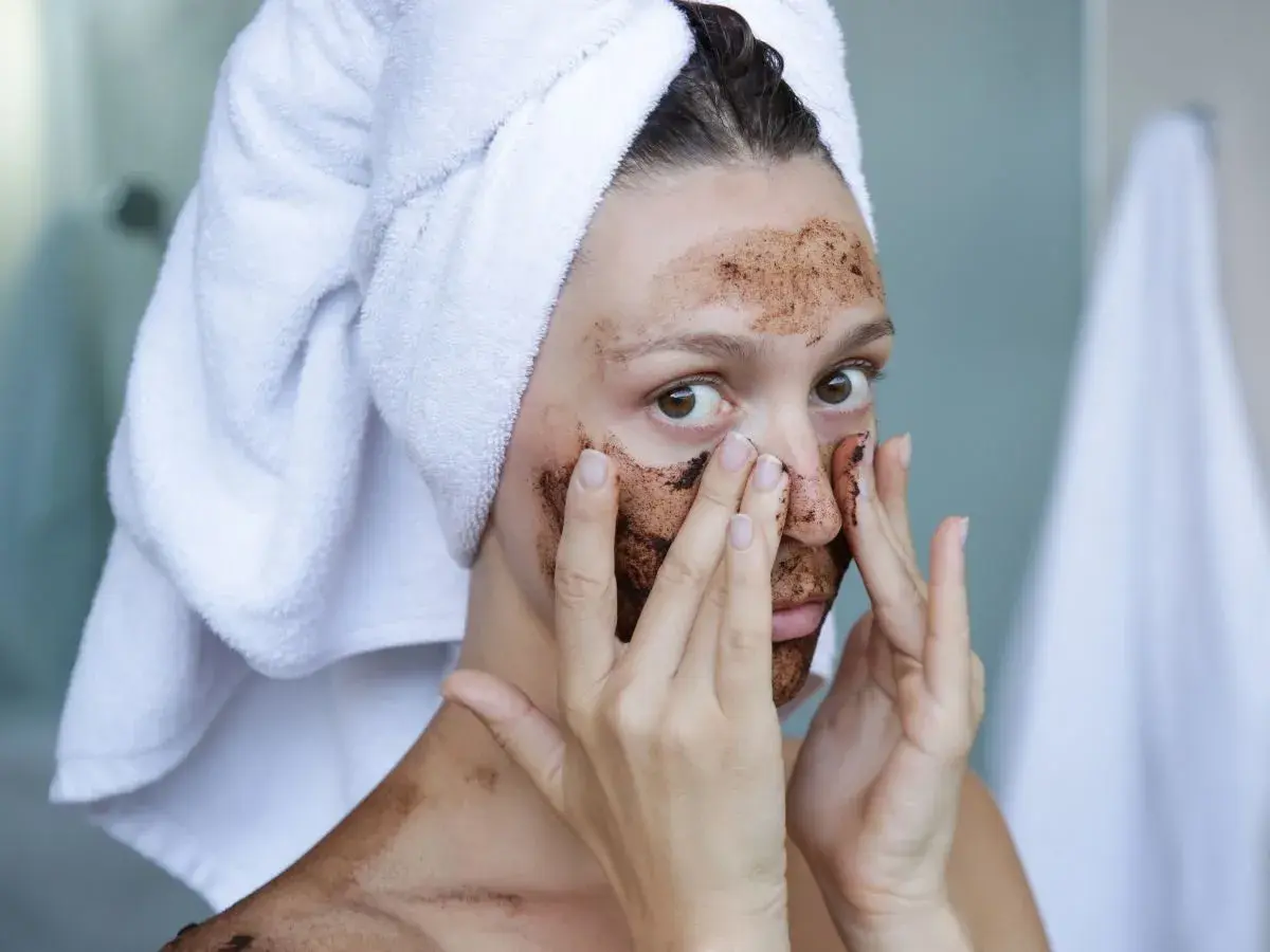 Kobieta z ręcznikiem na głowie nakłada na twarz domowy peeling złuszczający do twarzy.