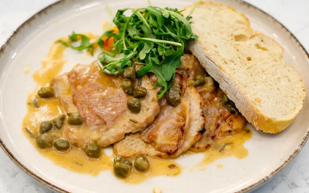 Pyszne saltimbocca alla romana z cielęciną, szynką, szałwią i kaparami w sosie, podane z rukolą i chlebem.