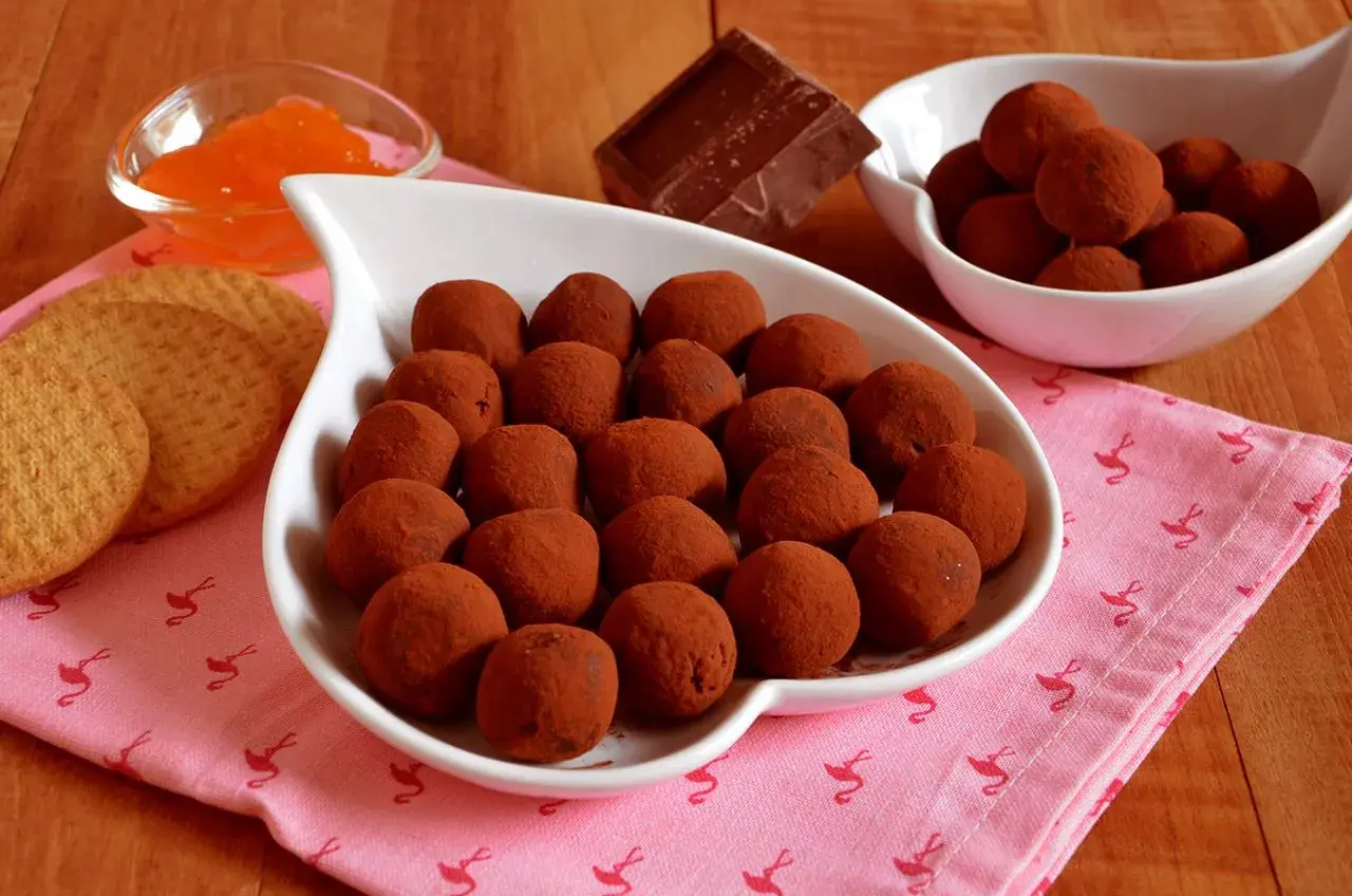 Bon bon cioccolato e panna anni '80, un dolce ricordo. Praline al cacao su un piatto bianco, con biscotti e marmellata d'arancia.