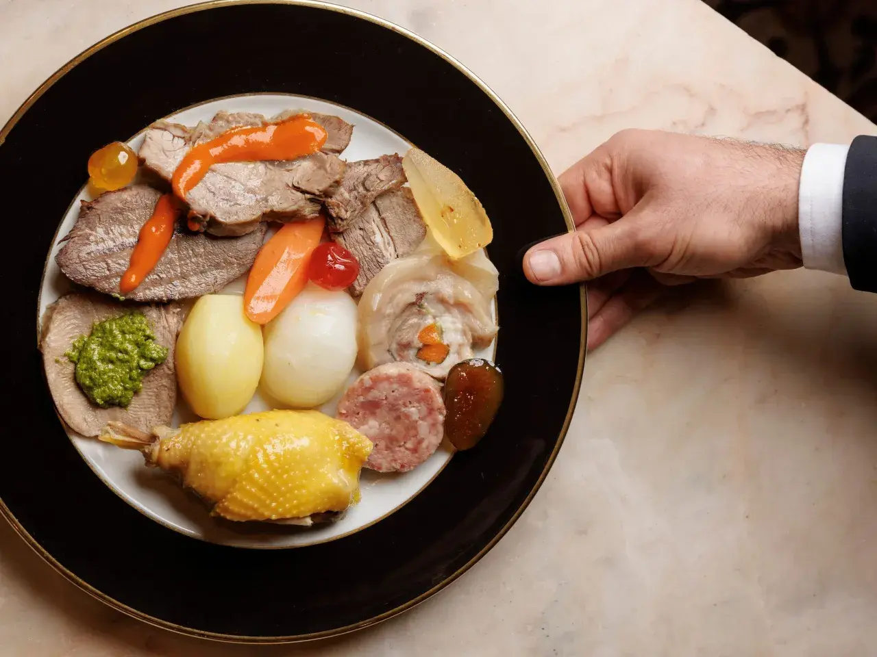 Un piatto ricco di bollito di carne, con verdure, salumi e un pollo arrosto, pronto per essere gustato.