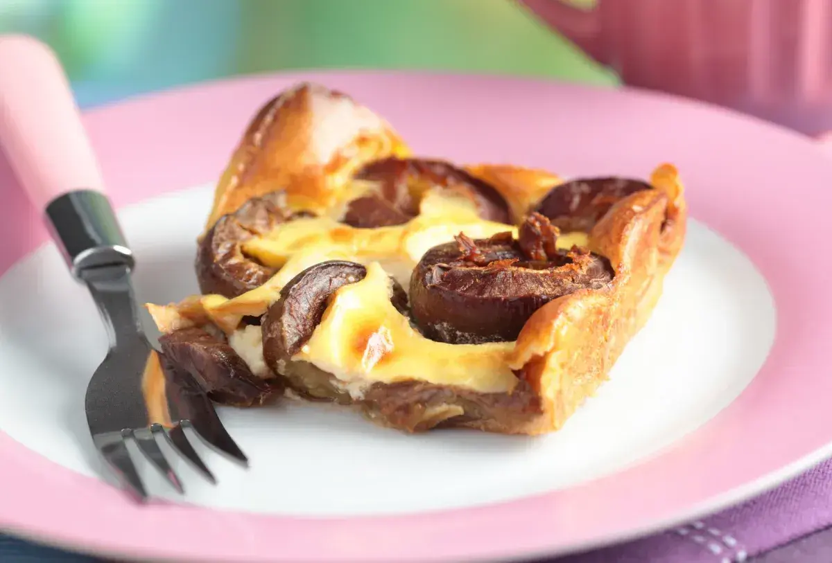 Tranche de clafoutis aux prunes moelleux sur une assiette rose avec une fourchette.