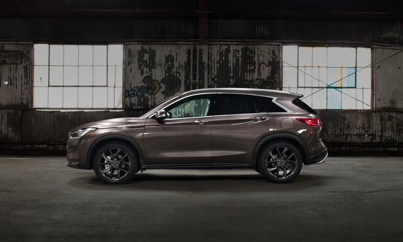 Brązowy Infiniti QX50 w profilu, zaparkowany w opuszczonym magazynie z graffiti na ścianach i dużymi oknami.