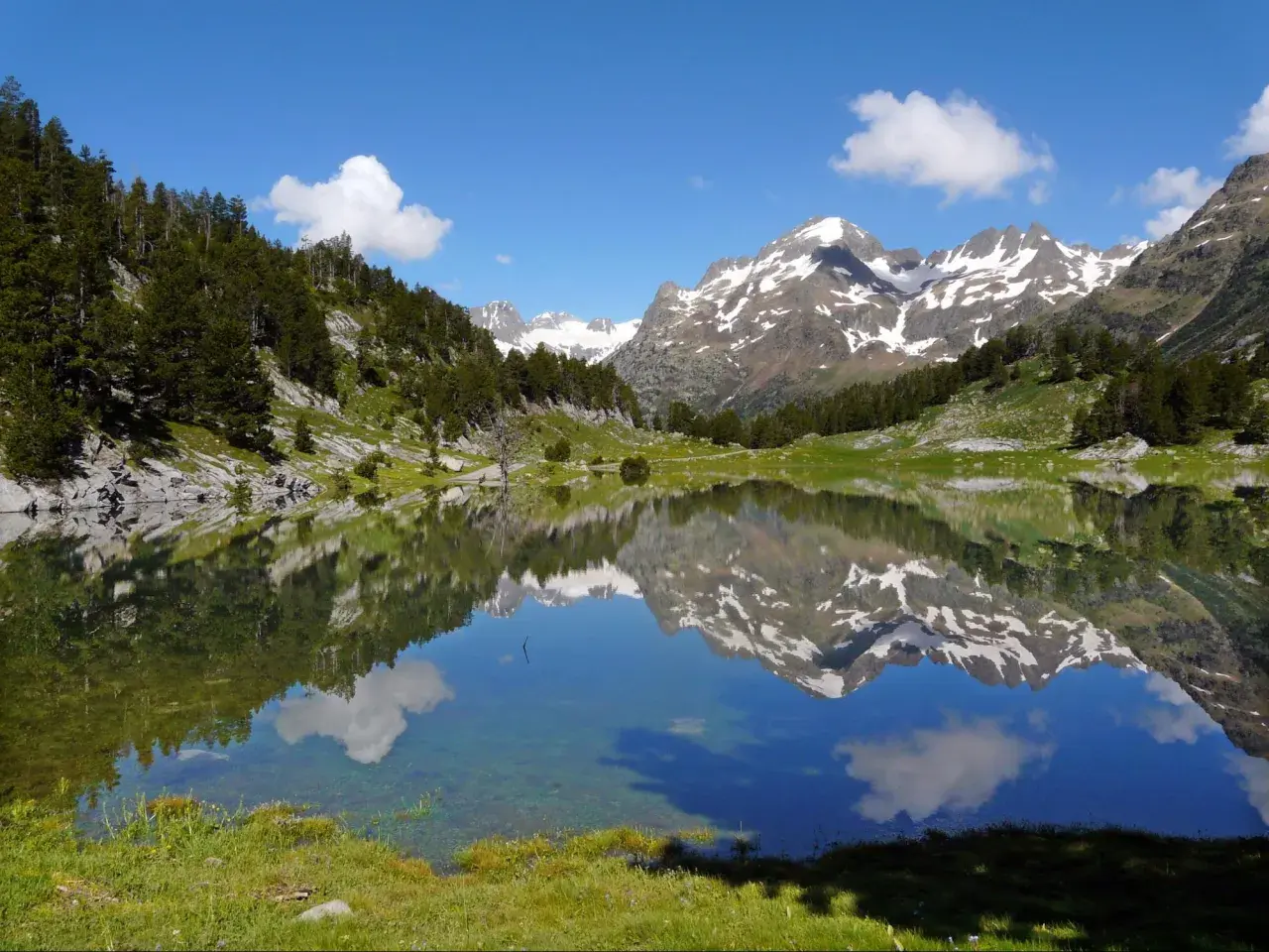 Espejo de agua en los valles de Huesca, reflejando montañas nevadas y un cielo azul con nubes.