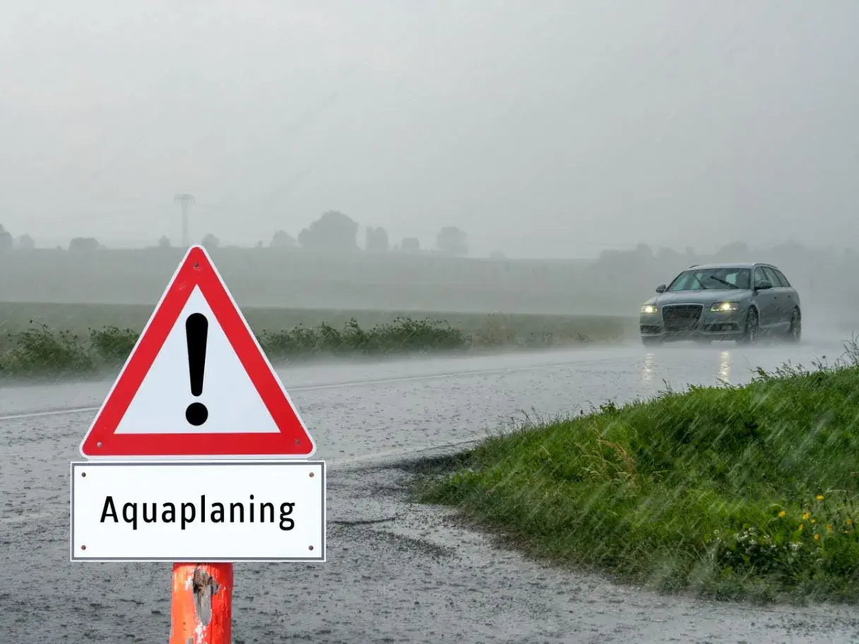 Señal de advertencia de aquaplaning en un día lluvioso. Un coche circula por la carretera mojada. ¿Qué puede hacer para evitar el aquaplaning?