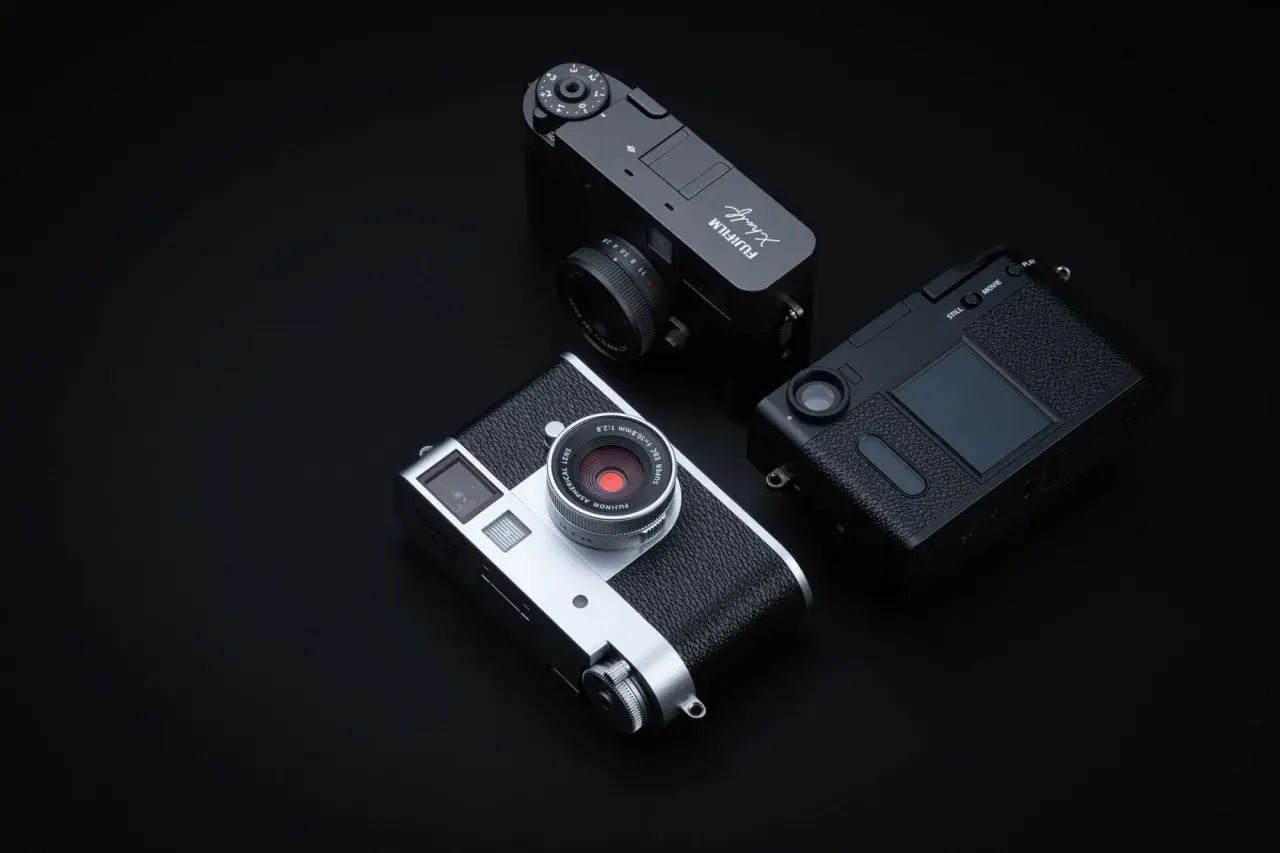 Tre fotocamere Fujifilm X-Half, una argento e due nere, disposte su sfondo scuro.