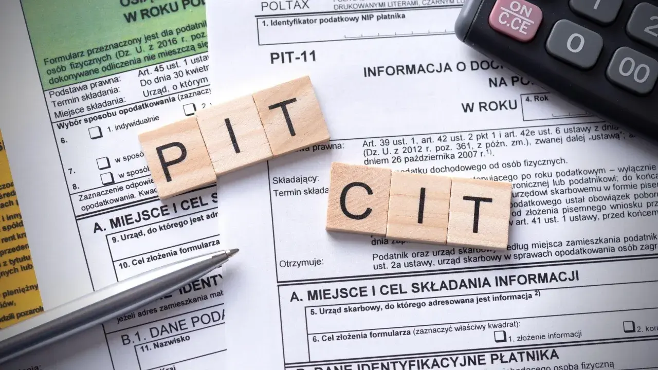Drewniane klocki z literami PIT i CIT leżą na formularzach podatkowych. Temat: podatek od sprzedaży nieruchomości po upływie 5 lat.