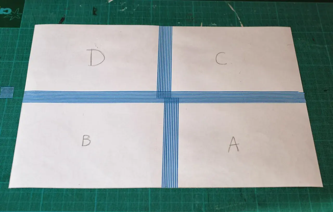 Papier divisé en quatre sections (A, B, C, D) par du ruban adhésif bleu rayé, prêt à créer un motif.