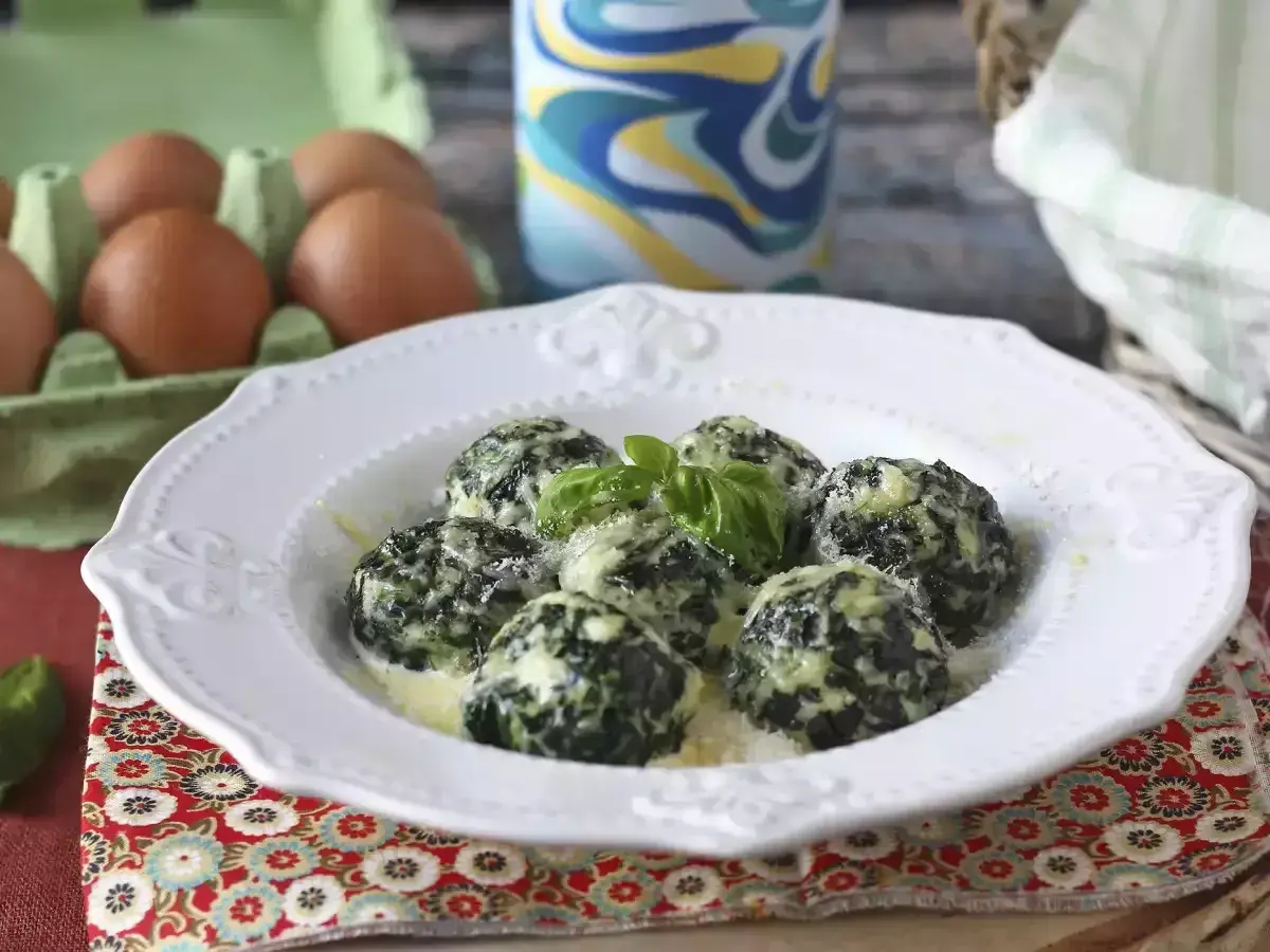 Spenat recept: Krämiga spenatbollar med basilika och parmesan på en vit tallrik. Ägg i bakgrunden.