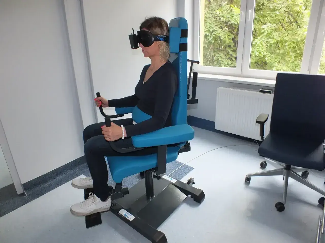 Kobieta w goglach VR na specjalnym fotelu wykonuje badanie vng. Gdzie zrobić takie badanie?