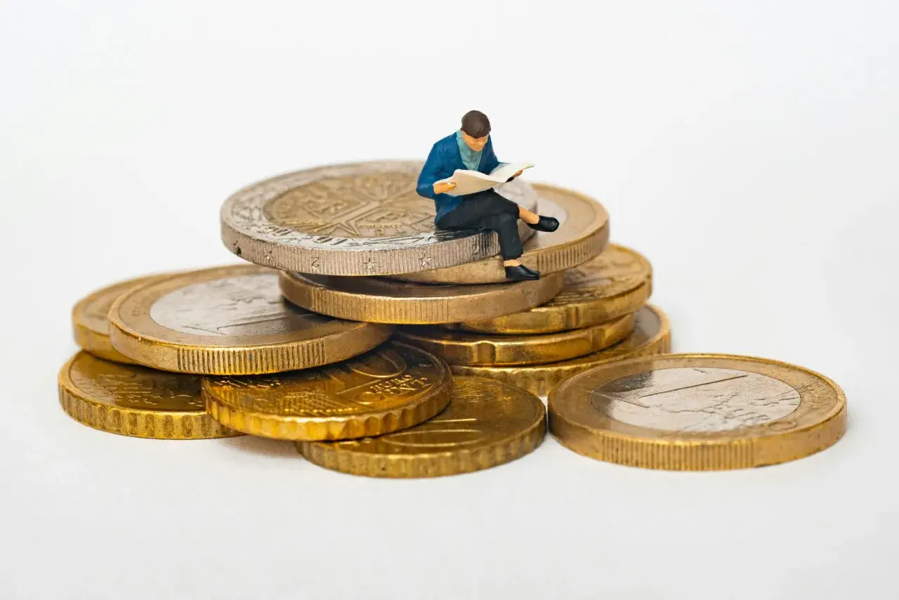 Figurka siedząca na stosie monet euro, czytająca gazetę. Symbolizuje eurocent pożyczki do domu.