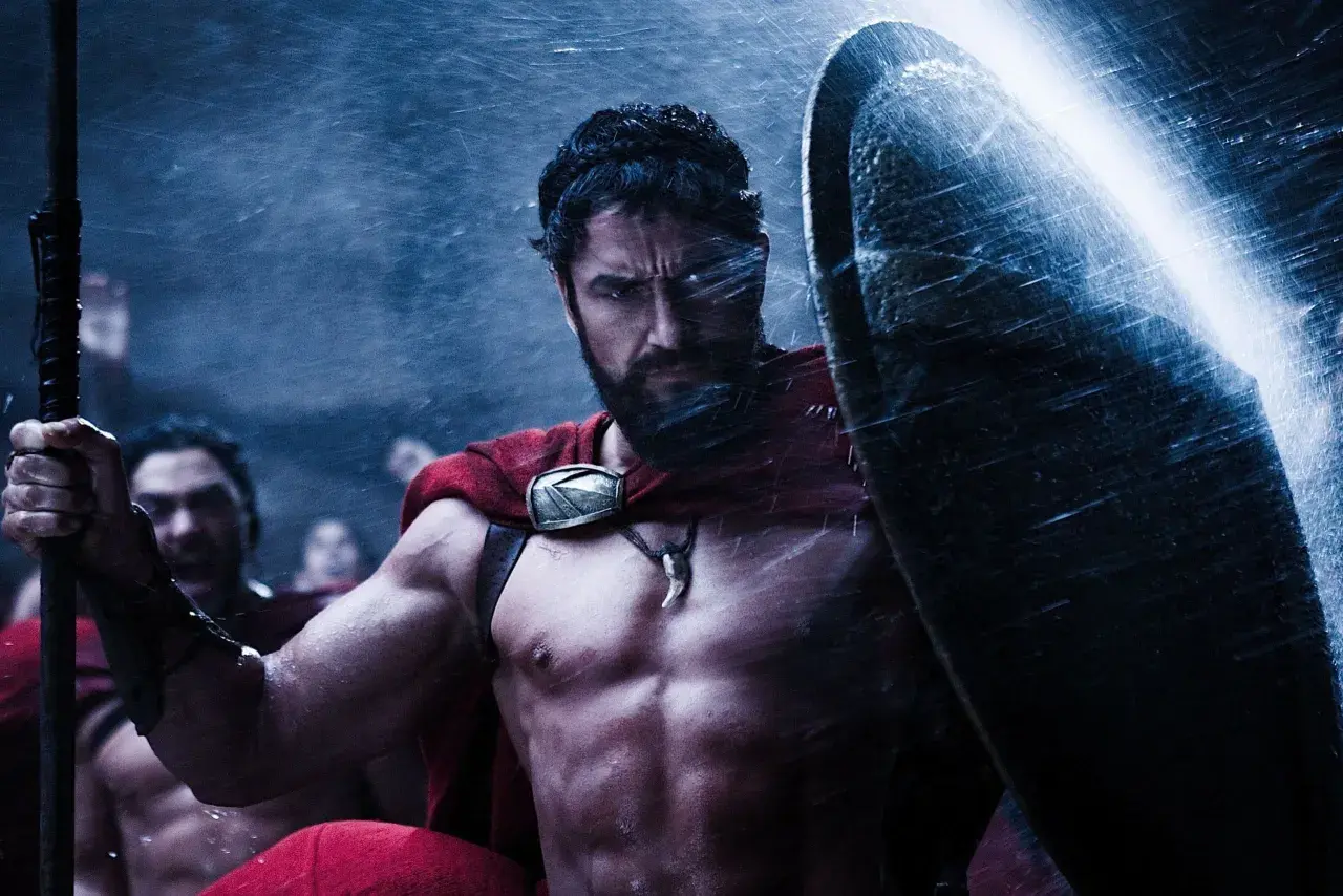 Gerard Butler jako Leonidas w filmach "300". Spartanin w deszczu, z tarczą i włócznią, gotowy do walki.