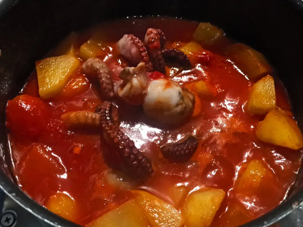 Un saporito stufato di polpo e patate in un sugo rosso brillante. I tentacoli del polpo sono ben visibili, immersi tra i pezzi dorati di patate.