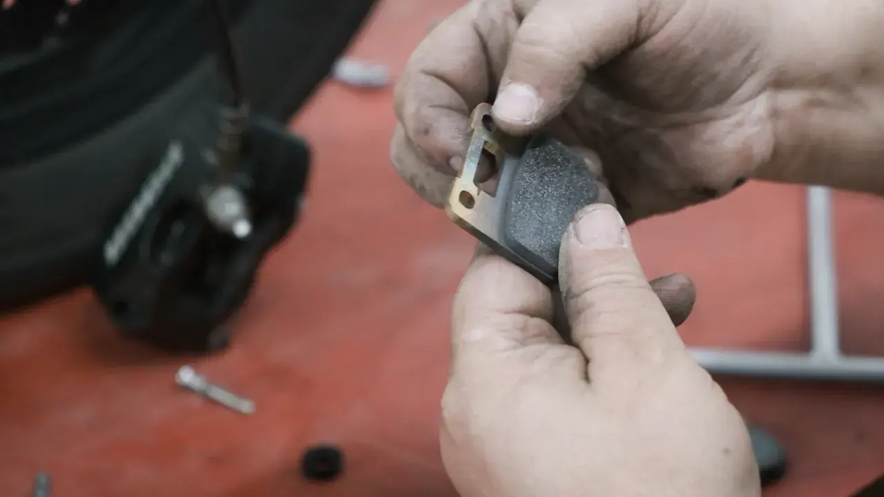 Manos sucias sostienen una pastilla de freno de moto lista para el cambio.