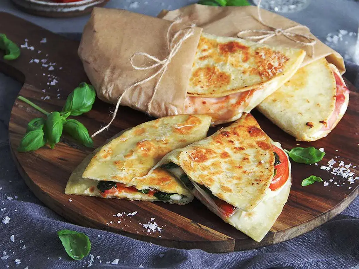 Läckra piadina recept på en träskärbräda, inslagna i papper med snöre. Basilika och flingsalt dekorerar.