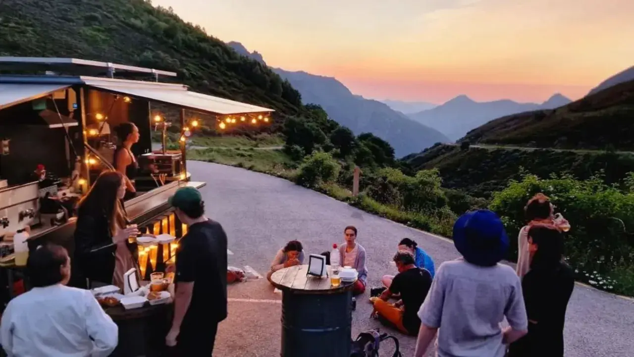 Gente disfrutando de comida y bebida en un food truck con vistas a montañas al atardecer. Un lugar ideal para descubrir los mejores pueblos para comer en Asturias.