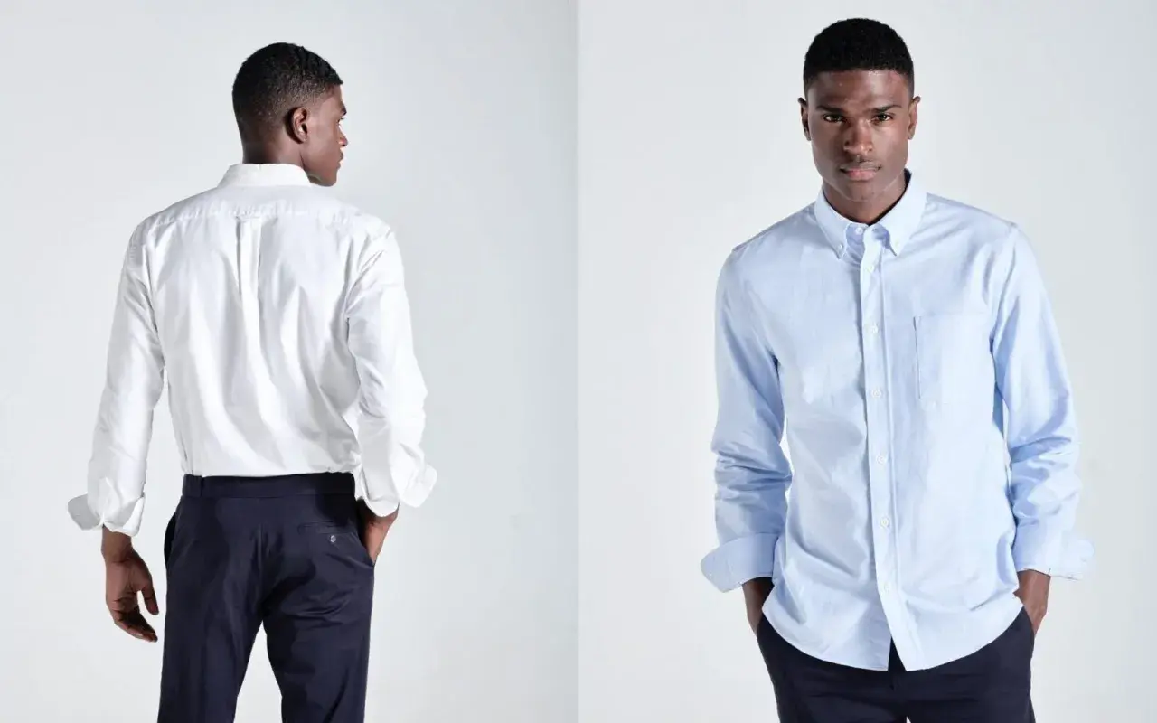 Ein Mann präsentiert ein weißes und ein hellblaues Button-Down-Hemd. Dieses Hemd mit Knopfleiste ist ein Klassiker.