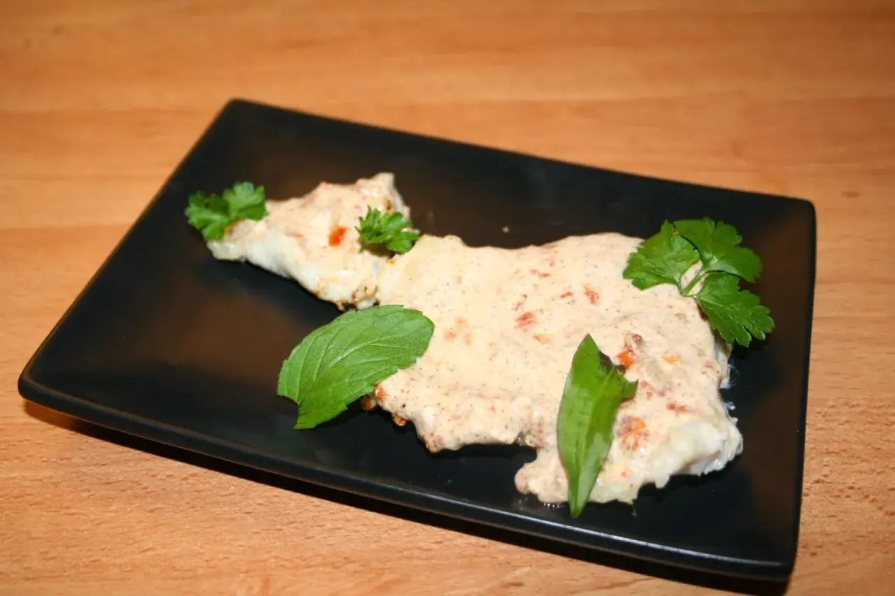 Zarter Fisch mit cremiger Joghurtsoße, garniert mit frischen Kräutern auf schwarzer Platte.