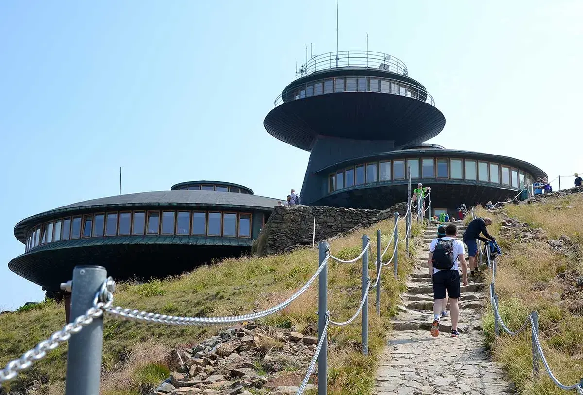 Wanderer steigen die Steintreppe zur Schneekoppe Seilbahn hinauf. Die futuristischen Gebäude auf dem Gipfel sind schon zu sehen.