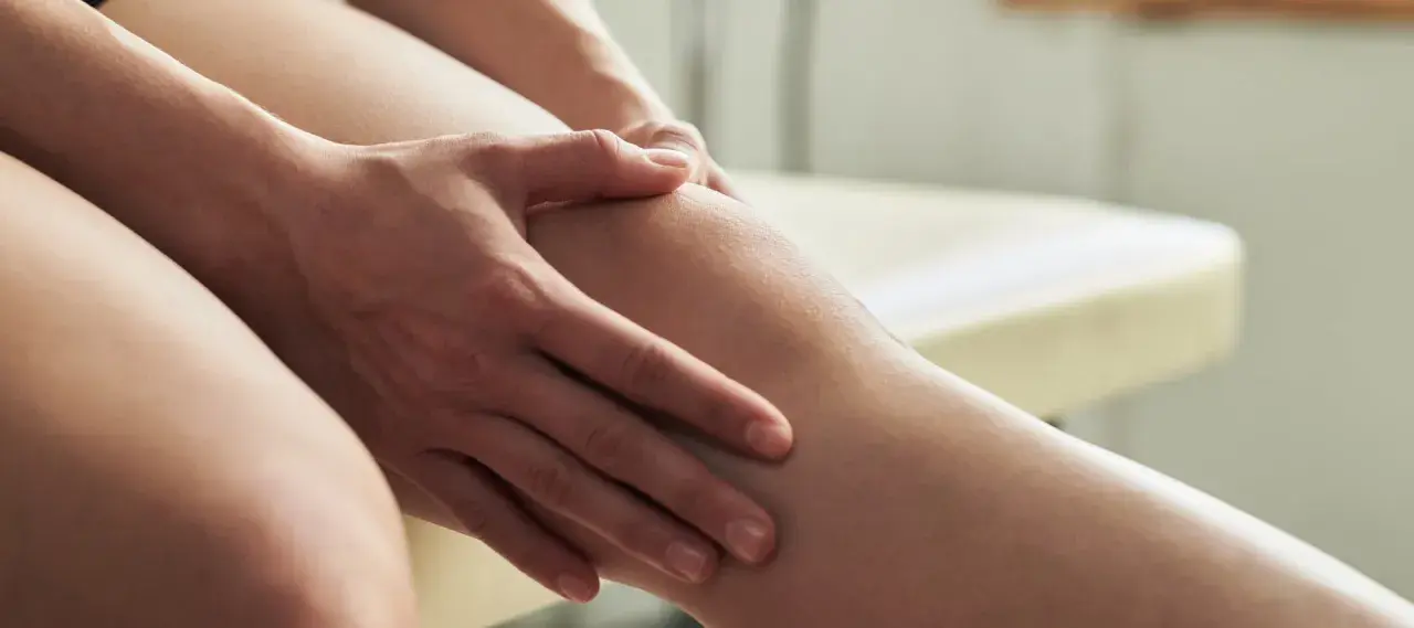 Hände massieren ein Bein, das nach dem Sport schmerzt. Magnesium hilft gegen Muskelkater.
