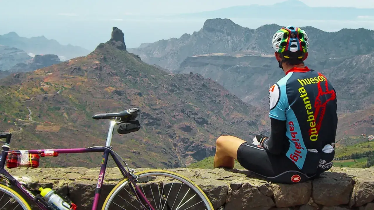 Ciclista descansa tras explorar rutas en bici Gran Canaria. Paisaje montañoso y su bicicleta morada.