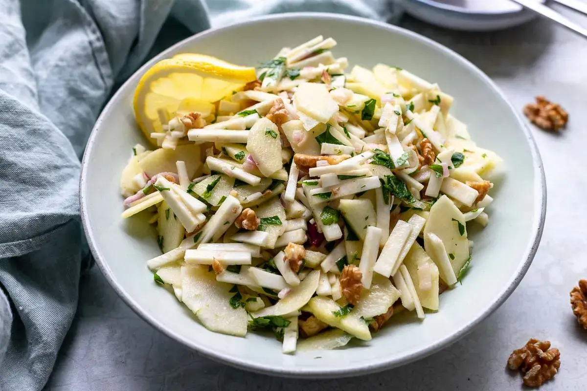 Ein frischer Staudensellerie Salat italienisch mit Äpfeln, Walnüssen und Kräutern, garniert mit einer Zitronenspalte.