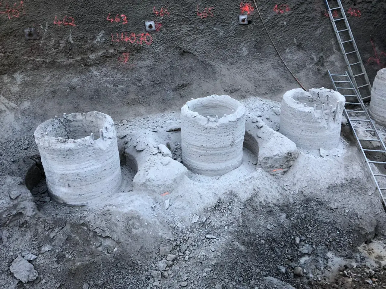 Bohrpfähle ragen aus dem Erdreich, die Reste einer tangierenden bohrpfahlwand. Eine Leiter lehnt an der Wand.