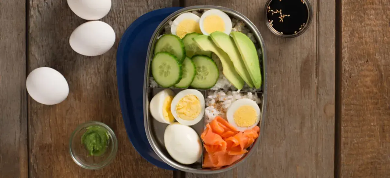 A bento box filled with rice, sliced cucumber, avocado, smoked salmon, and hard-boiled egg.