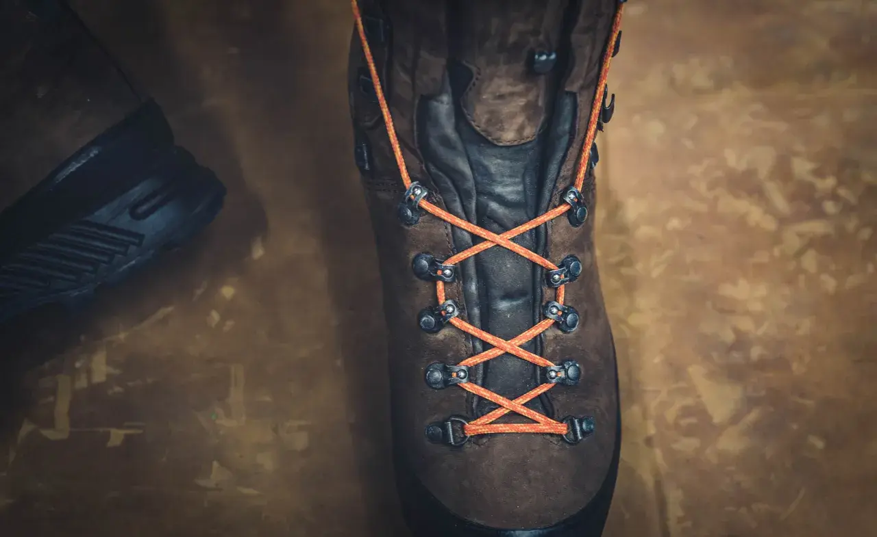 Close-up of a brown hiking boot with bright orange laces tied in a parallel lacing pattern, ready for adventure.