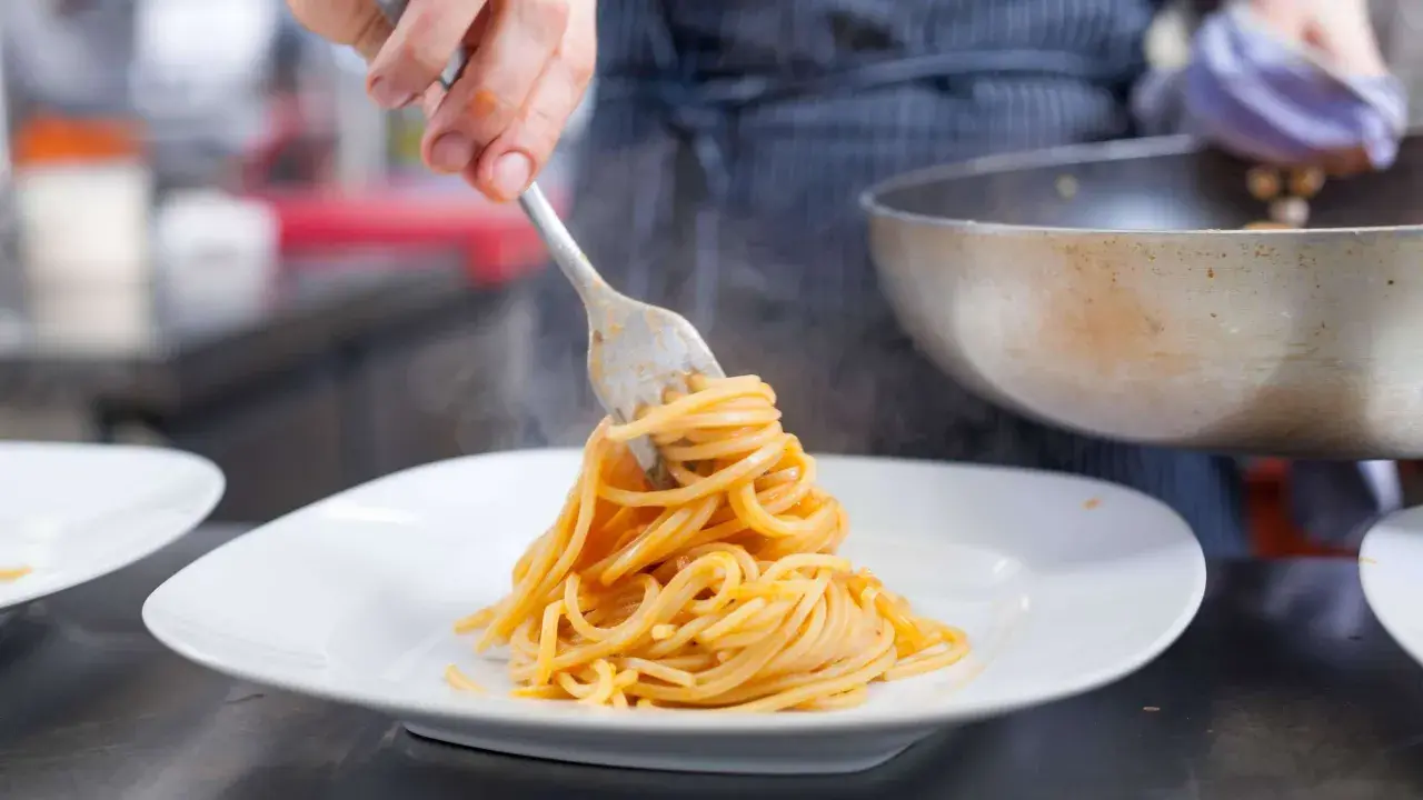 Eine Gabel hebt dampfende Spaghetti, ein Klassiker der Pasta italiana, auf einen weißen Teller.