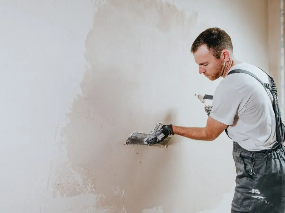 Operaio con spatola applica intonaco su muro. La rasatura è un passaggio cruciale per una finitura perfetta.