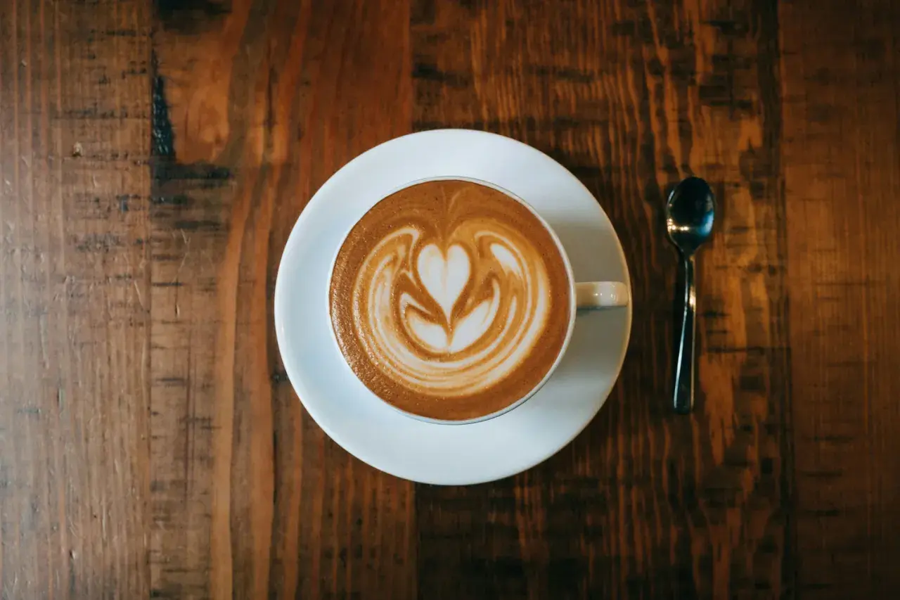 Ein Cappuccino mit Herz-Latte-Art auf einem Holztisch. Woher kommt Cappuccino? Aus Italien, natürlich!