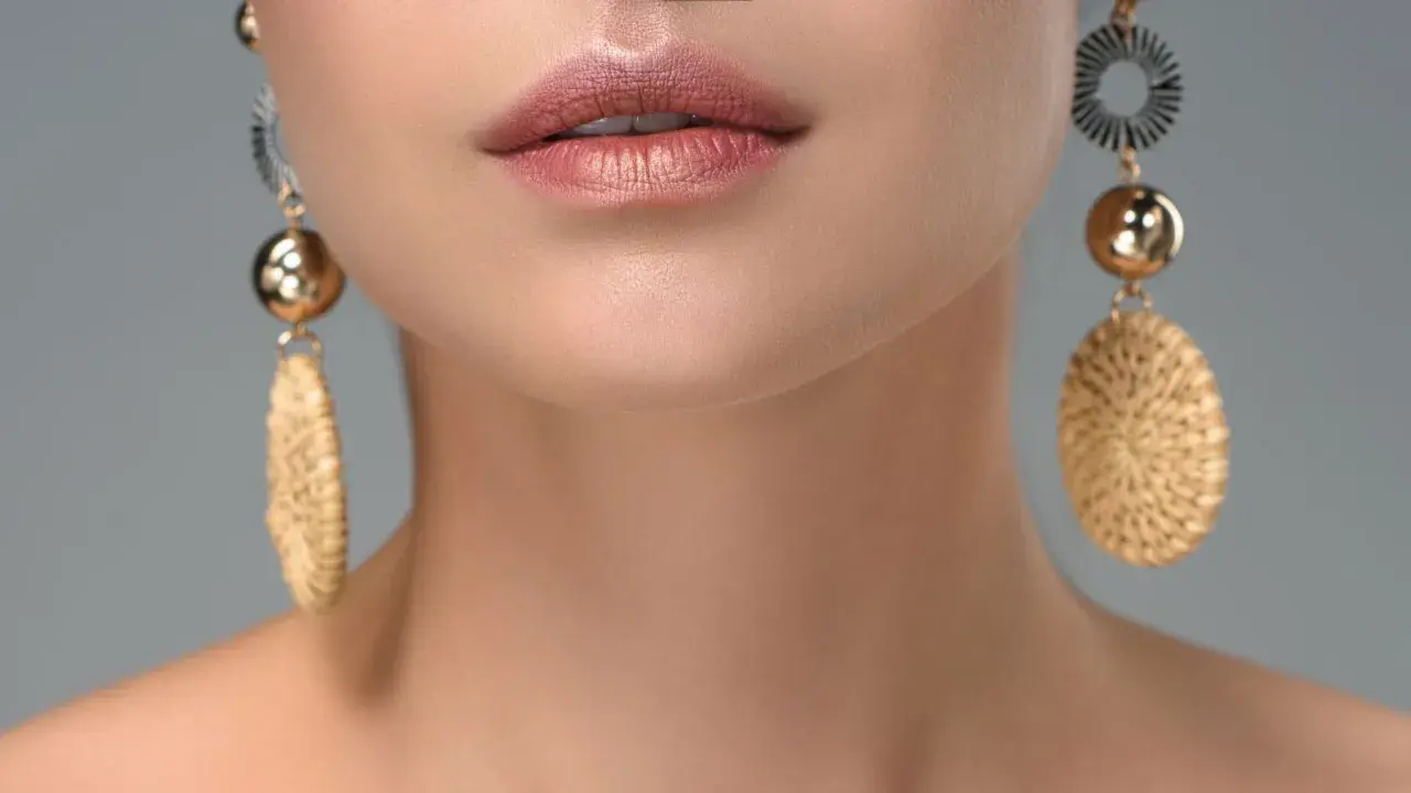 Labios maquillados y pendientes dorados con detalles que recuerdan a tipos de piedras preciosas.