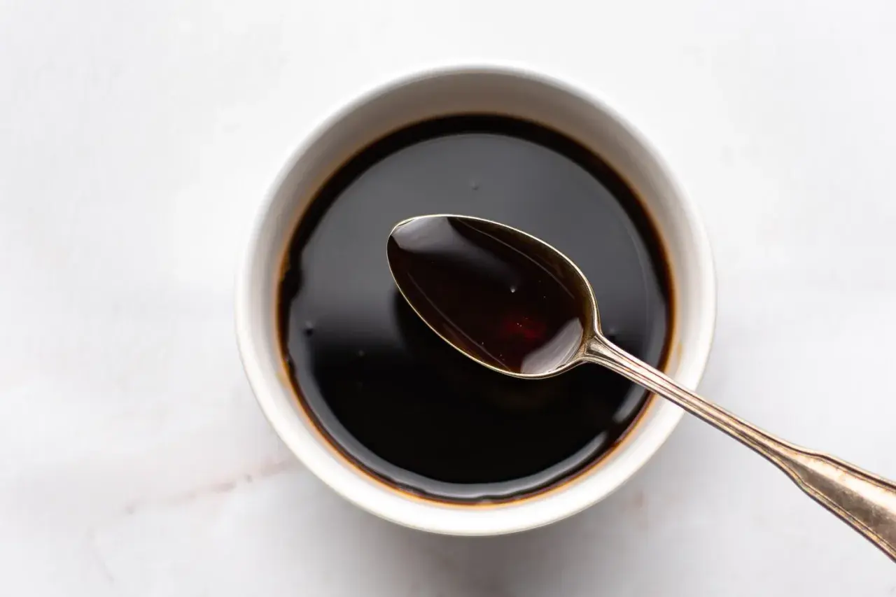 A spoon rests in a bowl of dark liquid, hinting at how to make sweet soy sauce.