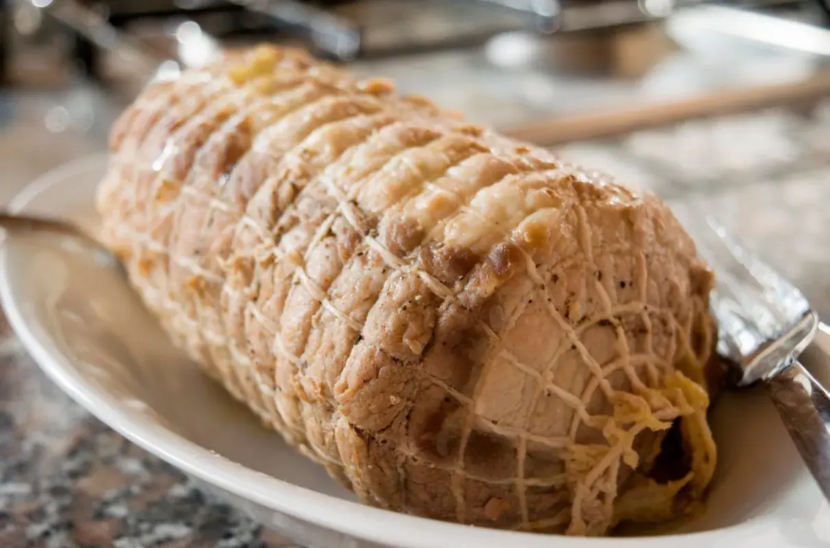 Gotowana szynka w siatce, gotowa do podania. Wygląda apetycznie, jakby była pieczona w majonezie.