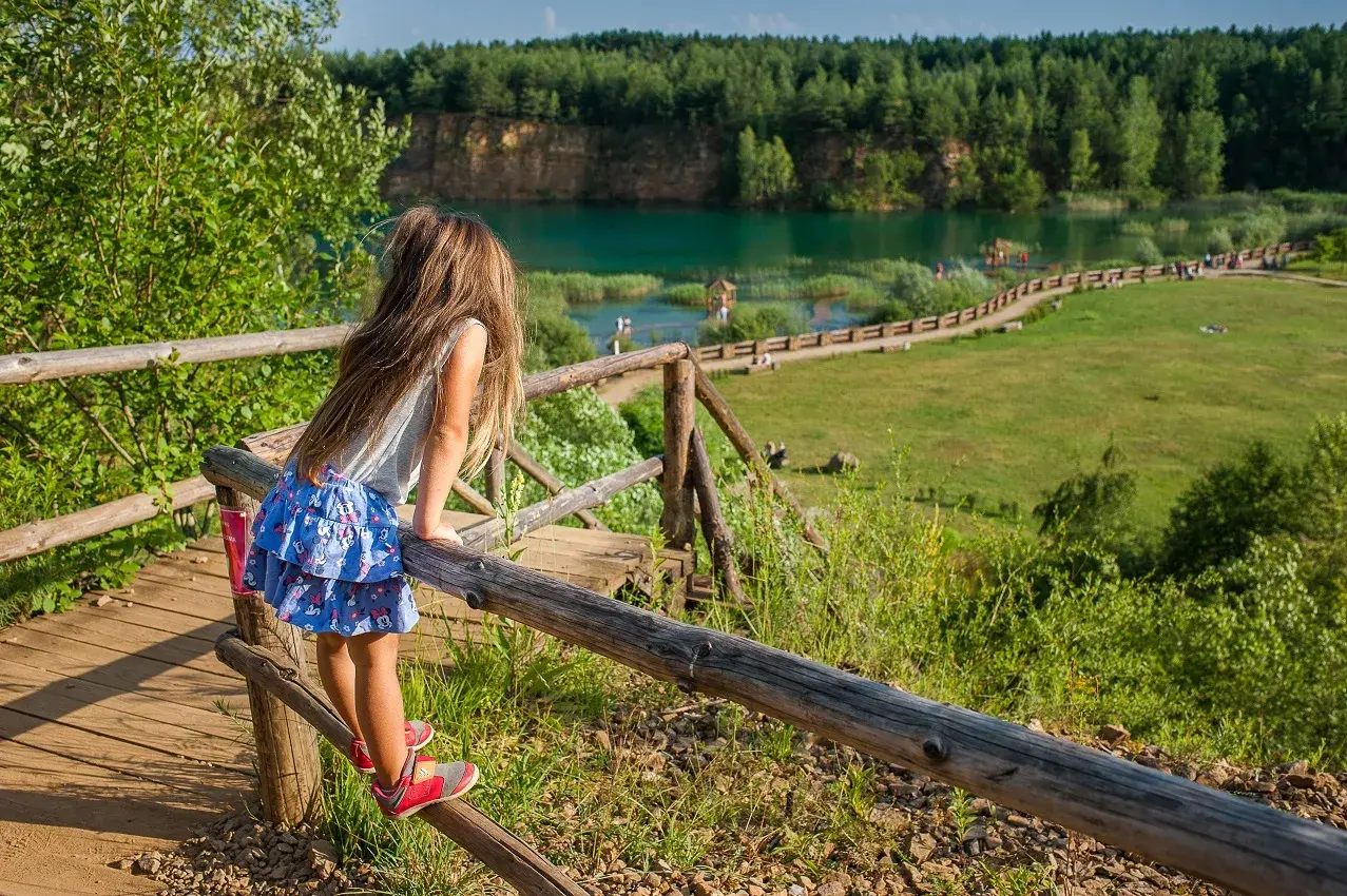 Dziewczynka na drewnianej kładce podziwia turkusową wodę i zieleń. To polskie Malediwy w Jaworznie, idealne miejsce na letni relaks.