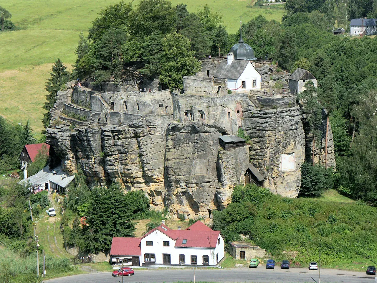 Felsenburg Einsiedlerstein thront auf einem Sandsteinfelsen, umgeben von grünen Hügeln und Wäldern.