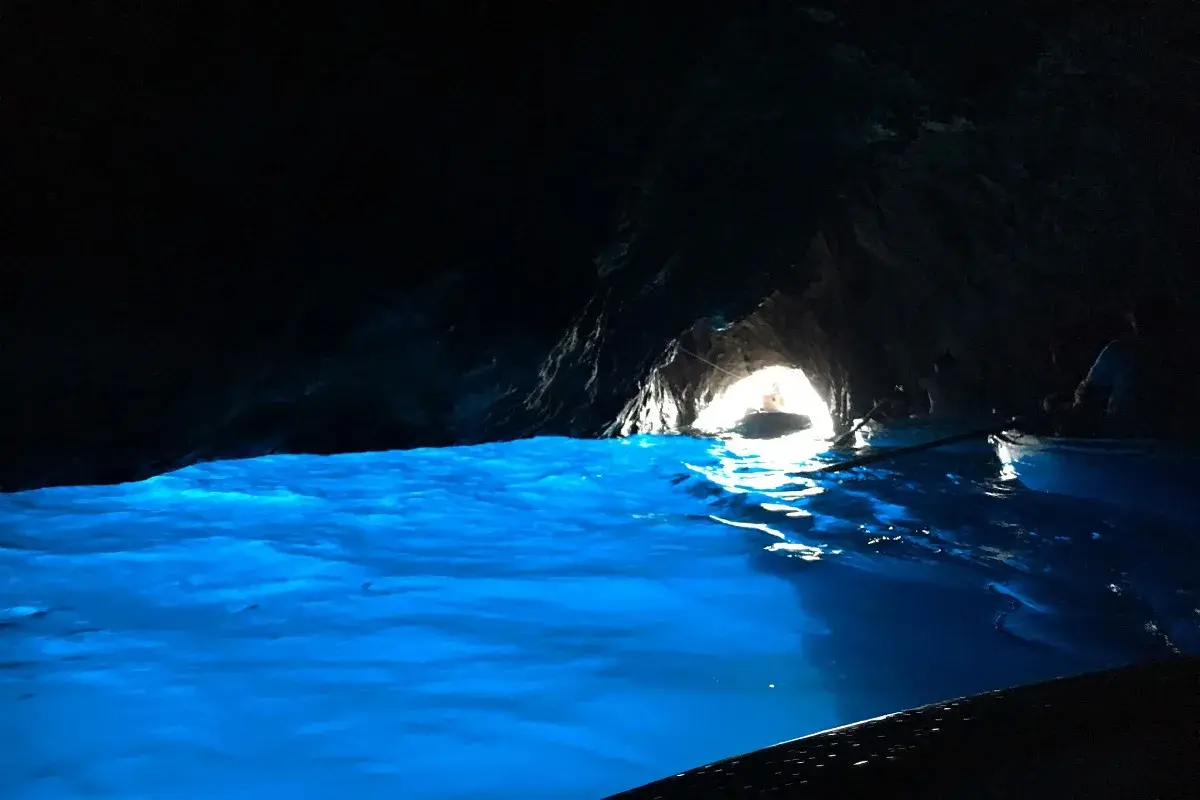 Acqua azzurra e luminosa in una grotta buia, con un'uscita illuminata dove si intravede una barca.
