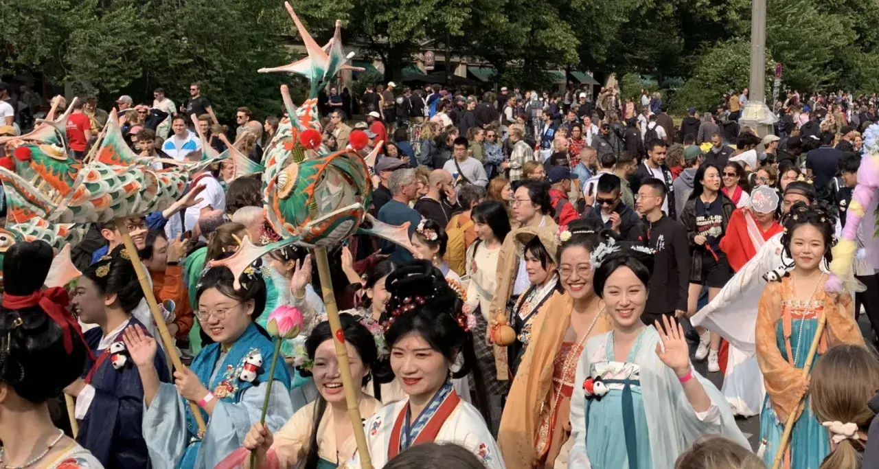 Bunte Drachenköpfe und Menschen in traditionellen Gewändern beleben den **Carnival Berlin**. Eine fröhliche Parade zieht durch die Menge.