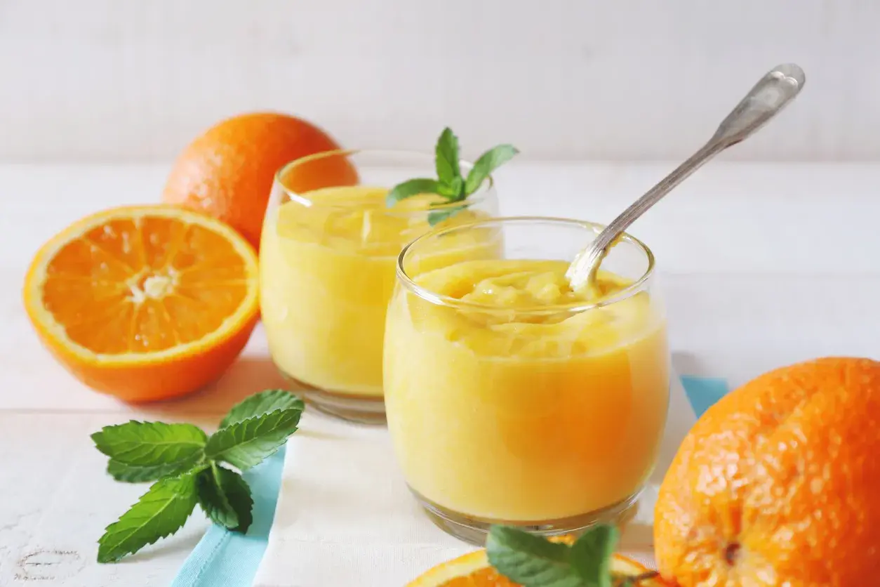 Dwa szklanki orzeźwiającego, gęstego **orange curd** z miętą i świeżymi pomarańczami.