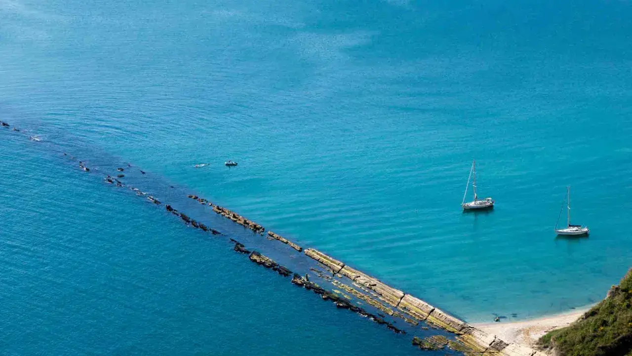 La spiaggia del Trave, con le sue acque turchesi, ospita due barche a vela e un piccolo motoscafo.