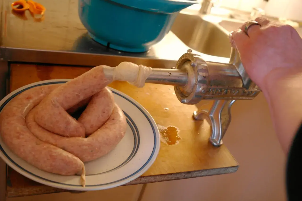 En hand vrider på en köttkvarn som gör korv. Ett korv-recept blir verklighet på tallriken.