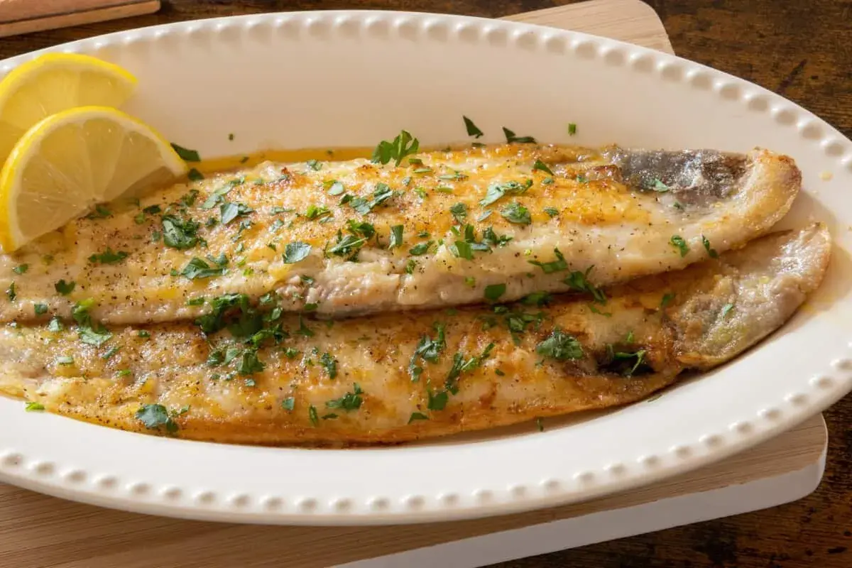 Delicioso lenguado a la plancha, dorado y jugoso, adornado con perejil fresco y rodajas de limón.