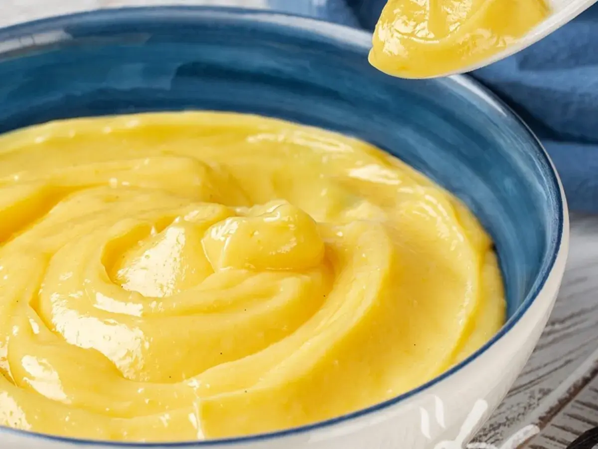 Una ciotola blu piena di deliziosa crema pasticcera vegana, con un cucchiaio che ne preleva una porzione.