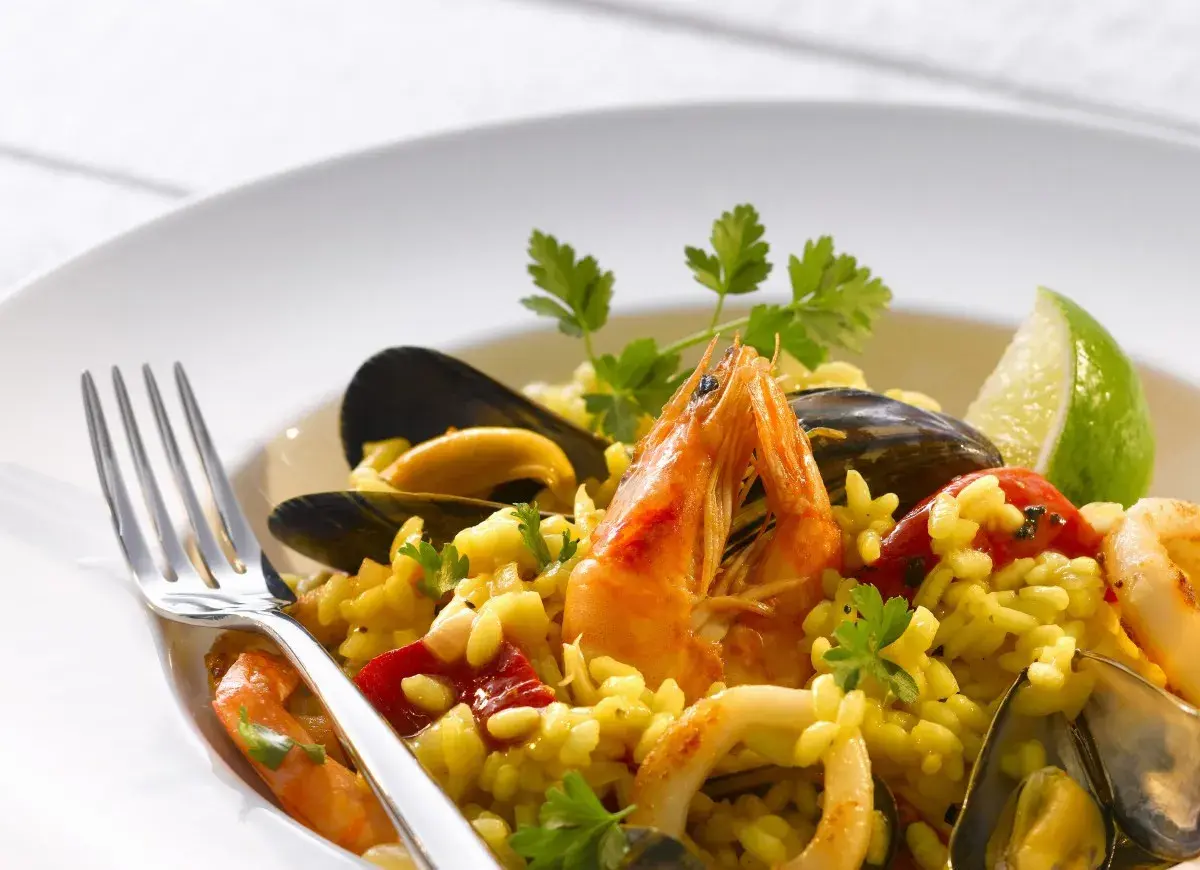 Pyszne risotto z owocami morza: krewetki, małże, kalmary i ryż, udekorowane natką pietruszki i ćwiartką limonki.